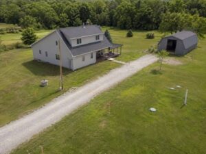 Aerial view of a rural property with a farmhouse, barn, well cap, septic markers, gravel driveway, and surveyed lot features.